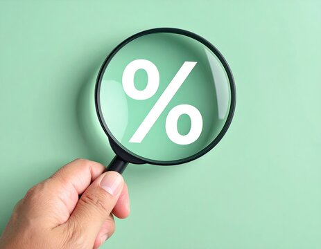 Hand holding a magnifying glass focusing on a white percentage sign against a light green background.