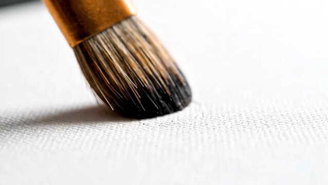 An artist's paintbrush makes first contact with a blank white canvas, ready for creation