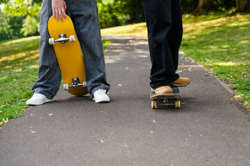 Teenagers enjoying a sunny day practicing skateboarding skills in a park with green trees and a smooth path