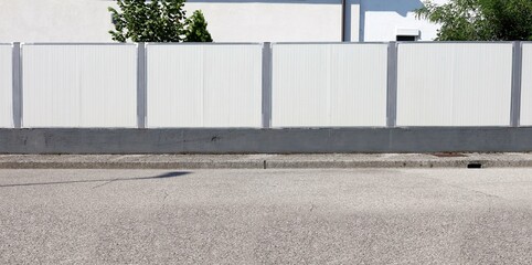 High white vinyl privacy fence on gray concrete base at the roadside. Sidewalk and street in front. Background for copy space.