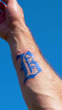 Arm with blue script-style tattoo against a solid bright blue backdrop, focused on the wrist and forearm