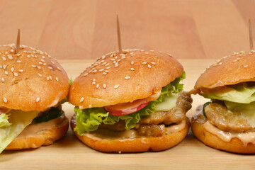 A side view of three fresh, homemade burgers with various toppings lined up on a rustic wooden board
