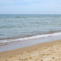 A tranquil horizontal view of a calm sea with gentle waves lapping the shore of a sandy beach. The composition is simple and balanced, providing ample copy space for text.
