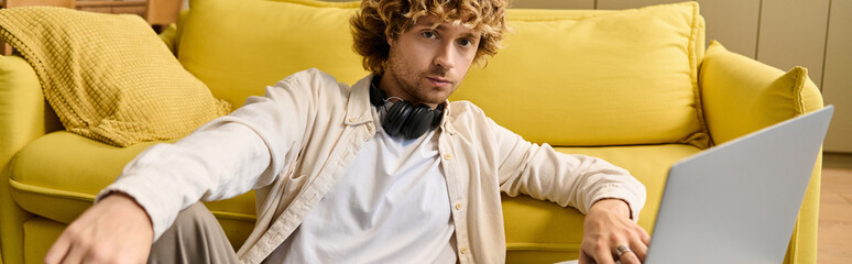 Charming young man relaxing on bright yellow couch while working on laptop