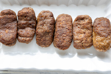 Close-Up of Romanian Mici Sausages Served with Flatbread and Tomatoes on a White Plate
