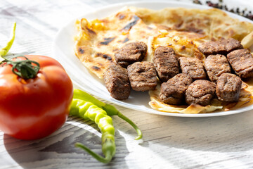 Close-Up of Romanian Mici Sausages Served with Flatbread and Tomatoes on a White Plate
