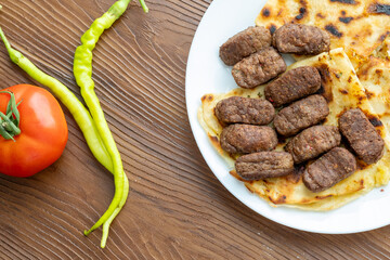 Close-Up of Romanian Mici Sausages Served with Flatbread and Tomatoes on a White Plate
