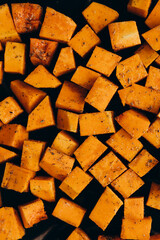 Pumpkin cubes in spices on the tray, prepared to bake, top view.