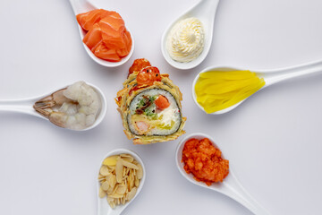 Sushi roll on a white background, and around it are white spoons with ingredients. Salmon, shrimp, tuna