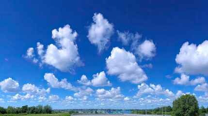 Obraz premium Expansive Blue Sky Vista Featuring Fluffy White Clouds with Natural Outdoor Backdrop Under Daylight Conditions and Green Vegetation in the Horizon