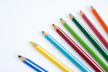 Сolored pencils lie in sharp focus against a soft-focus background on pure white surface, symbolizing children's educational creativity and artistic development during school lessons. 