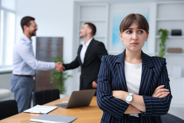 Woman feeling jealous of her successful colleague receiving congratulations in office, selective focus