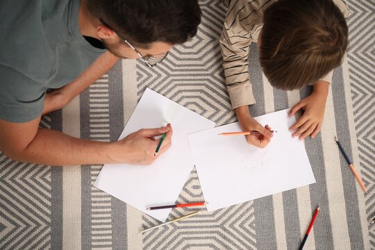 Father and son drawing together on floor at home, above view