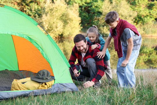 Happy father and his children setting up camping tent near river outdoors