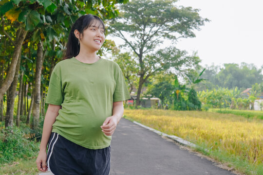 Beautiful young Asian pregnant woman doing morning jogging exercise, posing with nature background.