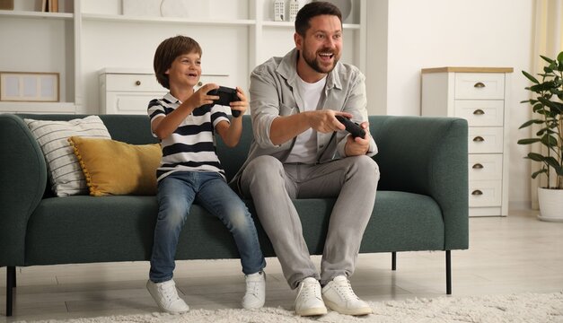 Father and son with controllers playing videogame on sofa at home