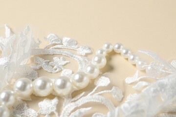 Beautiful pearl necklace and lace fabric on beige background, closeup