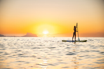 Young woman stand-up paddleboarding at ocean during sunset