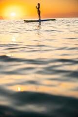 Young Caucasian woman stand-up paddleboarding at sunset