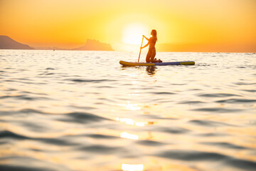 Young woman paddleboarding at ocean during serene sunset