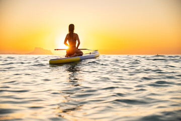 Young woman paddleboarding in serene ocean at sunset