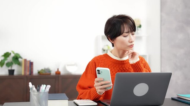 スマホとノートパソコンを見ながら悩むミドル女性