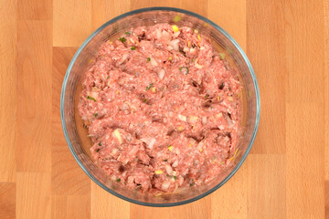 A horizontal, top-down studio shot of a glass bowl containing ground pork and beef mixed with onions and spices on a wooden background
