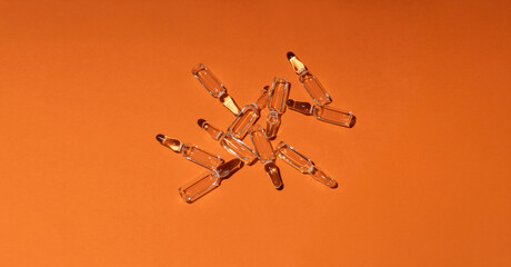 Set of glass ampoules on the bright orange background. Empty space. Vitamin C, E or beauty injections