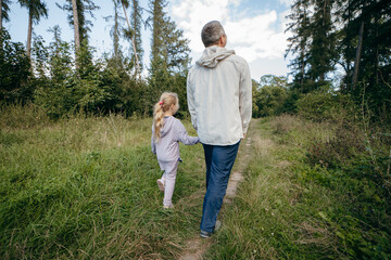 Fototapeta premium Adult father and little daughter are walking in the park