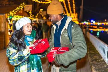 Happy multiethnic couple exchanging christmas gifts at market