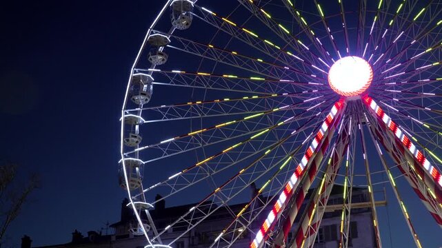 Vibrant ferris wheel rotating against a dark night sky in bayonne. Multicolored lights create a festive atmosphere, capturing the essence of christmas celebration in france