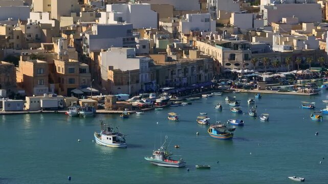 Malta, Marsaxlokk Harbour: Colorful Maltese luzzu boats creating a picturesque scene in the harbor of Marsaxlokk, a charming fishing village with vibrant buildings along the waterfront. Aerial shot