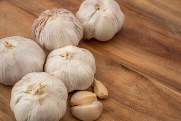 Five bulbs of garlic with several cloves placed on a wooden kitchen countertop, showcasing their natural texture and color in a well-lit environment.