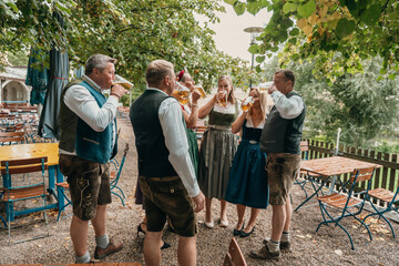 Cheerful friends in Bavarian costumes enjoy beer in a traditional beer garden in Bavaria Germany...