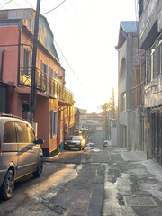 Fototapeta premium Urban photo. Winter morning city street. Cityscape with silhouette of two-story houses. Wallpaper with a village architecture. Slow life. Cars on the sidewalk. Rural views. Photo by phone. Nobody.