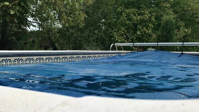 Gradual swimming pool solar reel thermal cover removal with lush greenery background