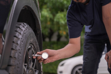Photo of a young man checking the air pressure in his car tires by himself.