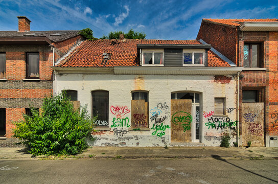 Wide shot of deteriorating residential architecture with boarded windows and street art under blue sky. Front-facing view shows urban exploration destination in Doel Belgium.