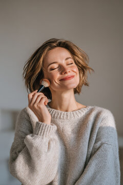 woman tenderly applying makeup with brush against soft milky background showcasing her morning routine