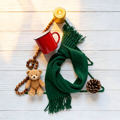 Cozy winter scene with scarf, teddy bear, mug, pine cone, and candle arranged as a Christmas tree decoration