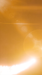Bright golden lens flare and sunburst effect creating soft glowing orbs on an amber background