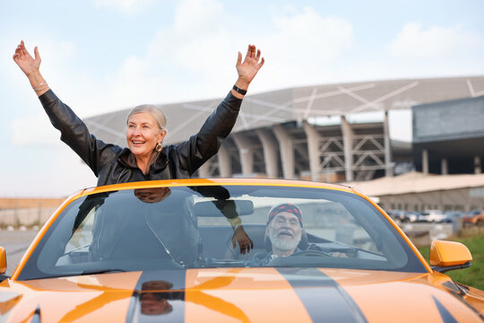Senior couple enjoying cabriolet ride in city. Woman with wide open arms