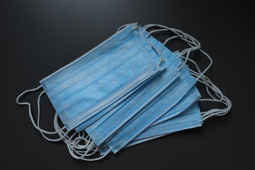 Set of blue disposable surgical masks with elastic ear loops lying on a dark background.
