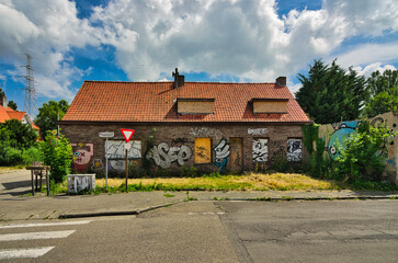 Wide shot of derelict residential building with boarded windows and vibrant graffiti murals under dramatic cloudy sky. Urban decay photography showing abandoned architecture in Doel Belgium.