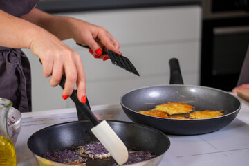 Hands of a chef skillfully flipping golden pancakes in frying pans, showcasing the cooking process of traditional potato snacks with fresh ingredients and vibrant colors with copy space