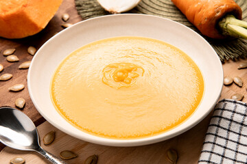 Pumpkin soup served on beige dish surrounded by ingredients