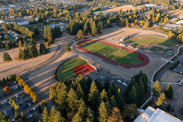 Aerial drone picture of college sports fields in Oregon City with soccer, baseball and track areas, students practicing on green lawns during fall sunset, surrounded by trees and campus buildings