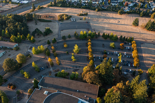 Aerial drone photo of an empty parking lot in Oregon City with landscaped rows, trees showing fall colors, and golden sunset light creating long shadows across the pavement and walkways