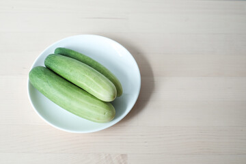 Fresh cucumber in white plate on the wooden table.
