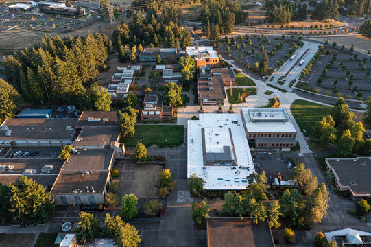 Aerial drone photo of a modern campus college area in Oregon City, USA, with surrounding trees and empty parking lots, captured during fall sunset with warm autumn colors and long evening shadows